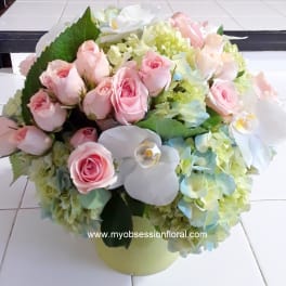 Pink roses and white orchids arranged with pale hydrangeas in a round vase