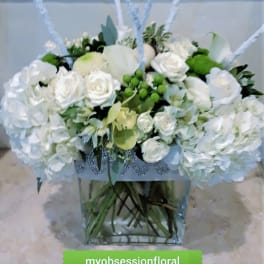 White rose arrangement in a clear square vase with green accents