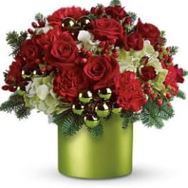 Round red and white flower arrangement with ornaments in a green cylinder vase with pine sprigs