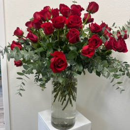 Red roses arranged in a clear glass vase with eucalyptus