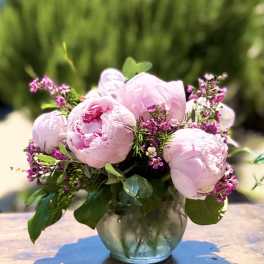 Pink peonies arranged in a glass vase with small purple filler flowers