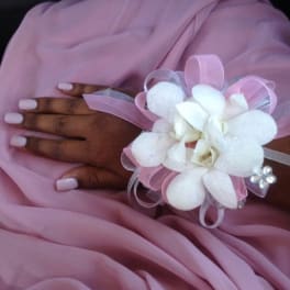 White floral wrist corsage with pink ribbon on a hand