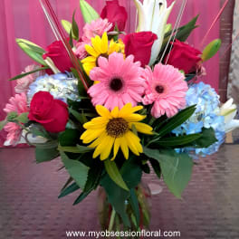 Mixed bouquet with roses, gerbera daisies, lilies, and hydrangeas in a glass vase