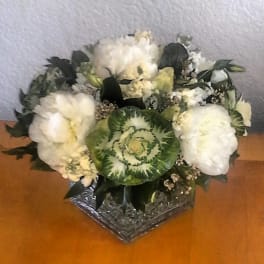 White floral arrangement with a green ornamental cabbage center in a glass vase