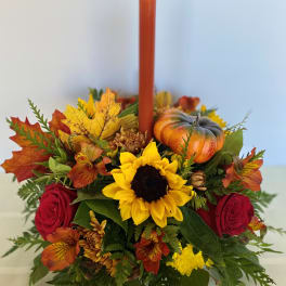Autumn floral centerpiece with a red candle, sunflower, roses, and a small pumpkin