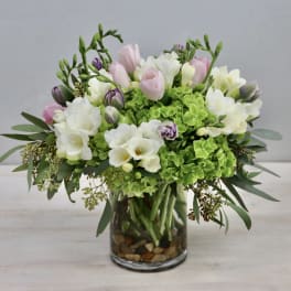 Pink and white flowers arranged in a glass vase with green blooms