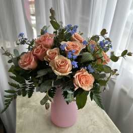 Peach roses and blue filler flowers in a pink vase