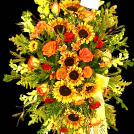 Tall floral standing spray with sunflowers and orange roses on a black background