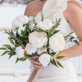 Bride holding a white peony bouquet with greenery and a trailing blush ribbon