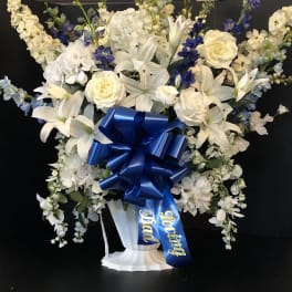 White and blue floral standing arrangement with a large ribbon on a pedestal vase