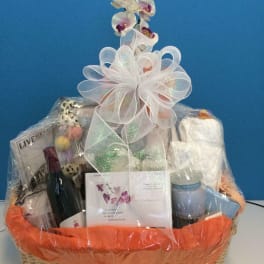 Gift basket with orchids, wine, a candle, and assorted items wrapped in cellophane