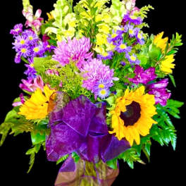 Colorful bouquet with sunflowers, purple daisies, and yellow snapdragons in a vase