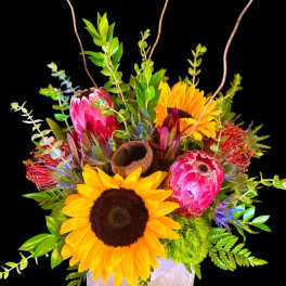 Sunflowers and pink protea in a square vase with greenery