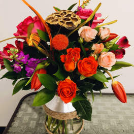 Mixed bouquet of orange, pink, and purple flowers in a glass vase