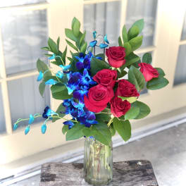 Bouquet of red roses and blue orchids in a glass vase