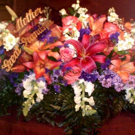 Large funeral spray with lilies, roses, and white flowers with gold script picks