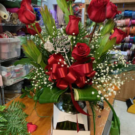 Red roses arranged with baby's breath and a red ribbon in a box.