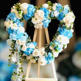 Heart-shaped floral wreath of white and blue flowers on an easel