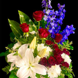 Bouquet of red roses, white lilies, and blue flowers in a low container