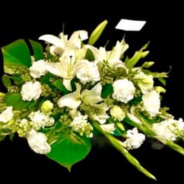 White lilies and carnations arranged with broad green leaves