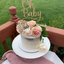 Small cake topped with pink and white roses and a glittery "Oh Baby" sign