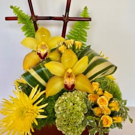 Yellow orchids and chrysanthemums in a brown container with bamboo accents