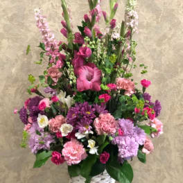 Tall pink and purple floral arrangement in a white woven basket