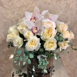Cream roses and white orchids arranged in a dark glass vase