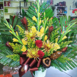 Tropical bouquet with yellow flowers, red roses, and large palm leaves in a white vase