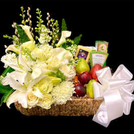 White floral arrangement in a woven basket with fruit and cheese boxes