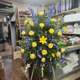 Tall floral spray with yellow roses and blue delphinium in a vase
