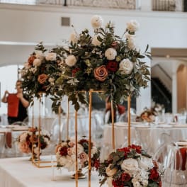 Tall floral centerpieces with roses and greenery on gold stands at a reception table