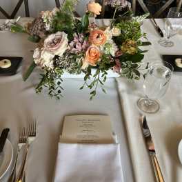 Low floral centerpiece with peach, blush, and white blooms on a dining table