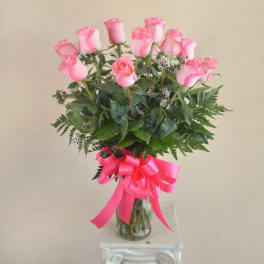 Pink roses arranged in a clear glass vase with a bright pink ribbon