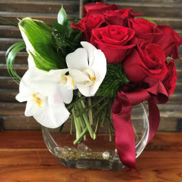 Red roses and white orchids in a clear glass vase with a burgundy ribbon