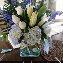 White tulips and blue flowers in a glass vase with blue beads