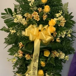 Standing floral spray with yellow roses and white blooms on a ribboned easel