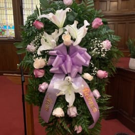 Large funeral wreath with white lilies, pink roses, and a purple ribbon bow