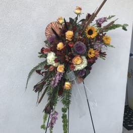 Tall floral standing spray with roses, sunflowers, and purple blooms