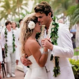 Bride and groom in white with floral leis and a white flower in her hair