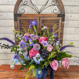 Mixed bouquet of pink and purple flowers in a blue vase with a ribbon