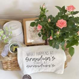 Pink rose plant in a basket with a printed towel and gift items
