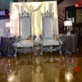 Two ornate silver thrones in front of a draped white backdrop
