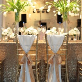 Tall white floral centerpieces on gold chairs at a decorated table