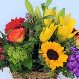 Mixed bouquet in a wicker basket with lilies, roses, sunflowers, and purple blooms