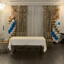 Event backdrop with gold sequin curtains, balloon columns, and a table