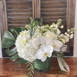 White floral arrangement with orchids, hydrangeas, and roses in a green vase