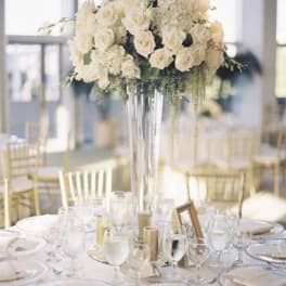 White rose centerpiece in a tall glass vase on a set dining table
