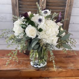 White bouquet with roses, hydrangeas, and dark calla lilies in a glass vase