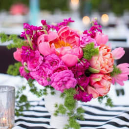 Pink and coral flowers arranged in a white vase on a striped tablecloth.
